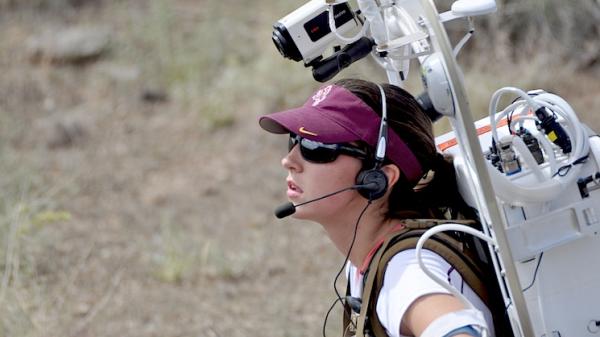 Kelsey stands with extraterrestrial geological field equipment strapped to her back.