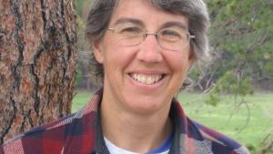 A close up of Ellen in a red plaid shirt, against a tree trunk.